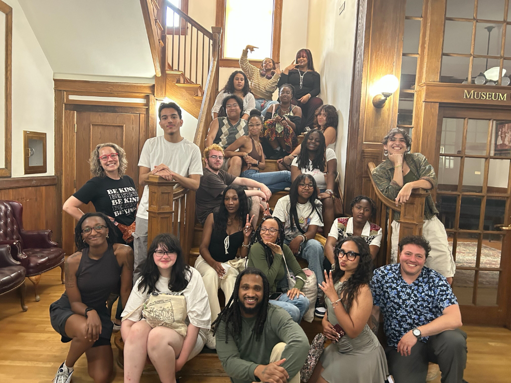 Twenty-one youth and adults from Deep's Action Research Team and Washington DC's Critical Exposure pose on a large wooden staircase. 
